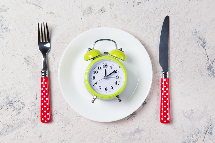 Alarm clock with bells on the plate with fork and knife, lunch time concept, top view with copy space